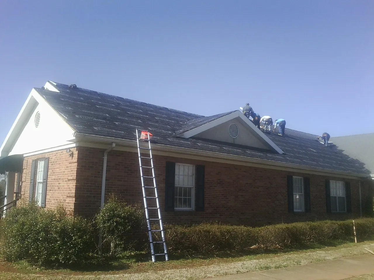 Crew tearing shingles off a brick ranch roof with a ladder set — Emergency Roof Repair work by our crew in New Salem