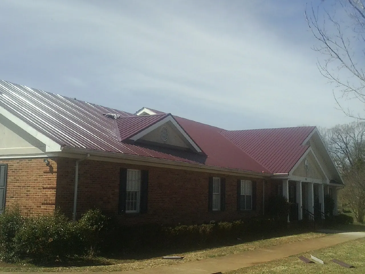 Red metal roof with gabled entries on a long brick building, from a Hail Damage Roof Repair job in New Salem