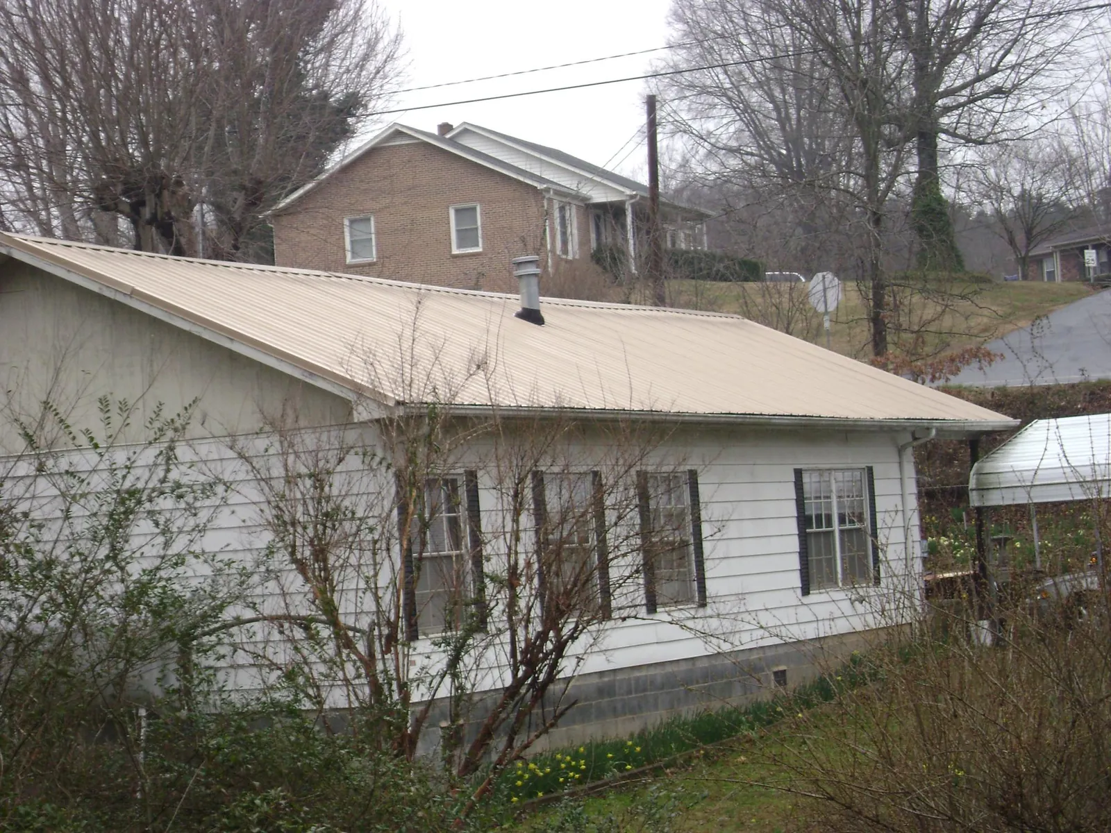 Tan metal roof on a white sided house set into a hillside — Commercial Roofing by Roofing Brothers in New Salem